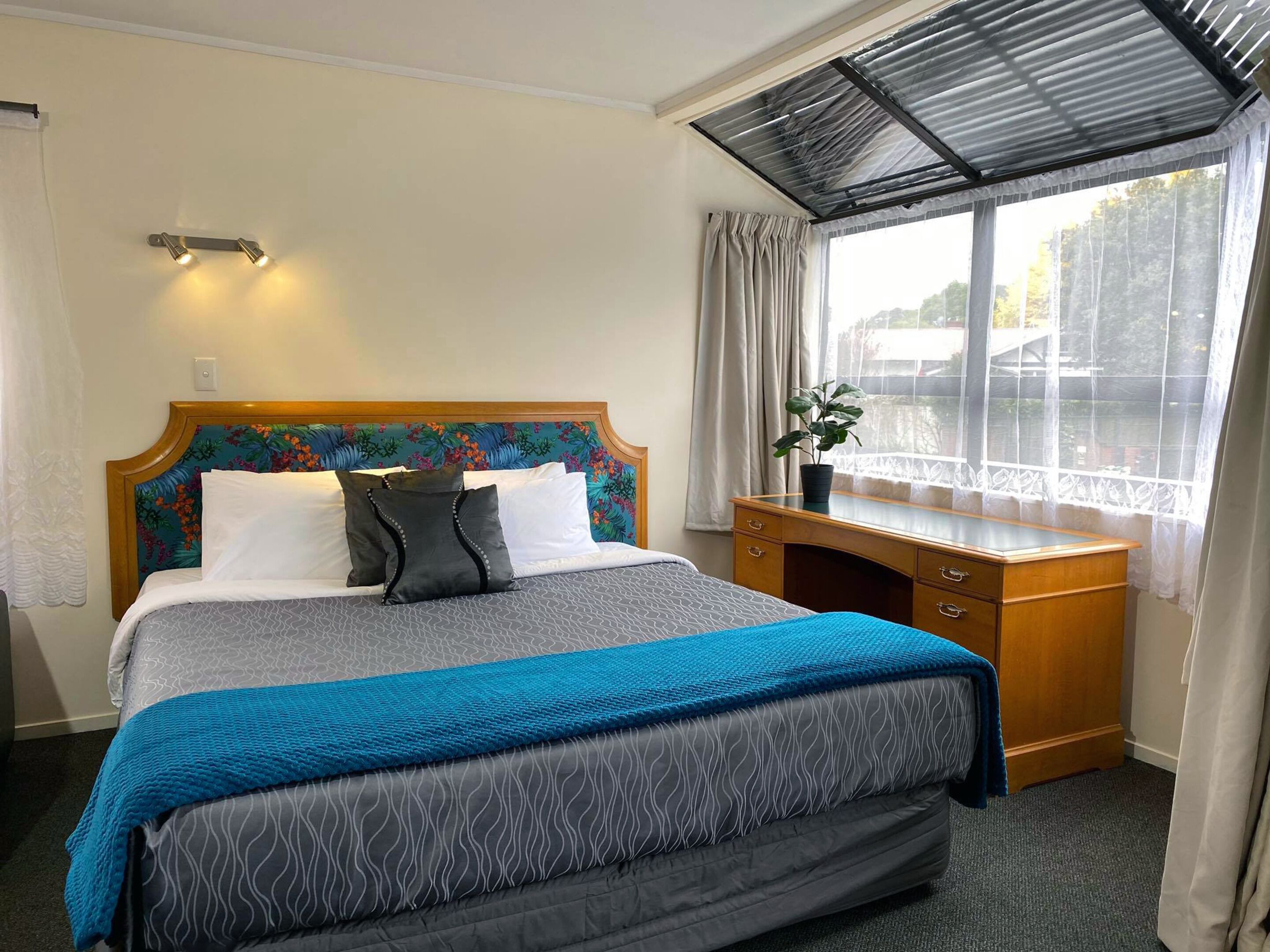 A hotel room with a bed, a desk, a window with curtains, and a view of the outside.