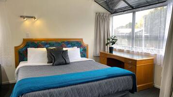 A hotel room with a bed, a desk, a window with curtains, and a view of the outside.