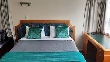 Quarto de hotel com cama, escrivaninha e janela com cortinas.