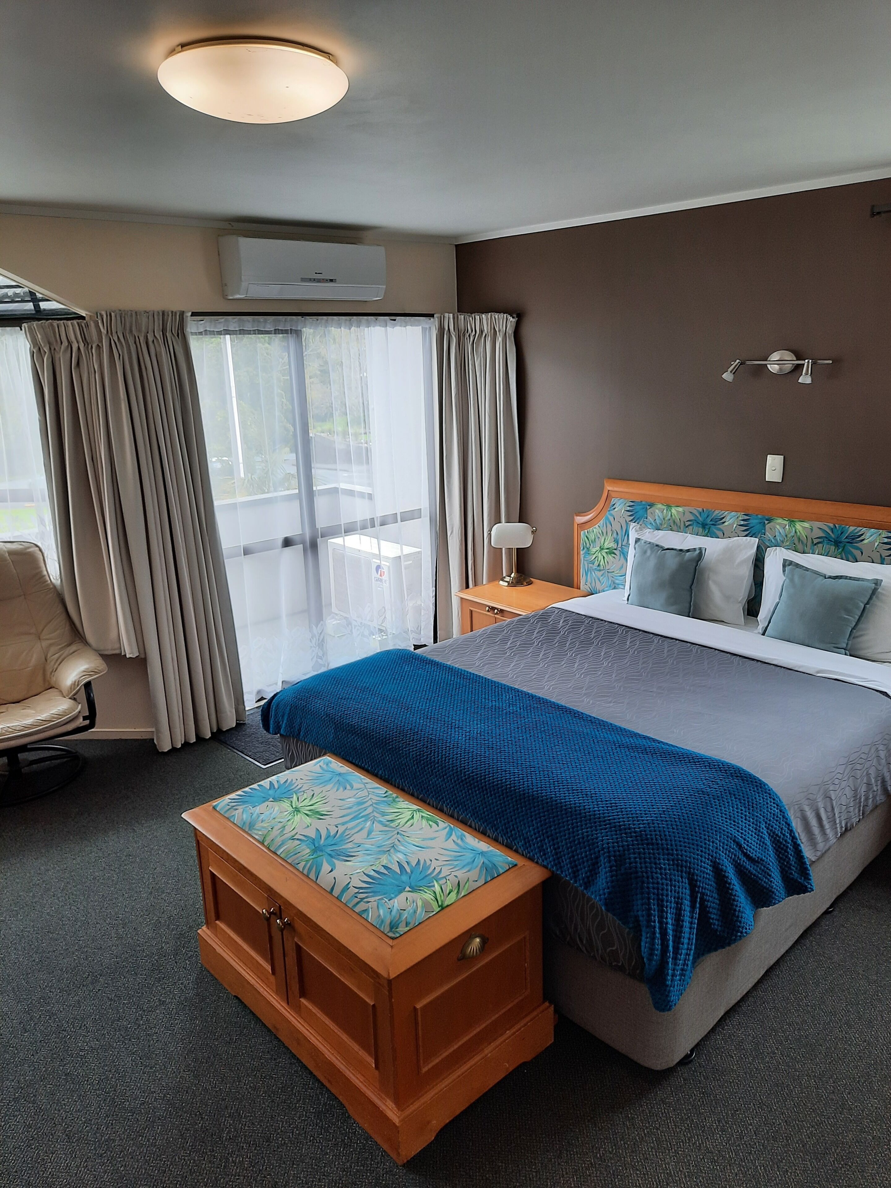 A hotel room with a bed, a chair, a desk, and a window with curtains.