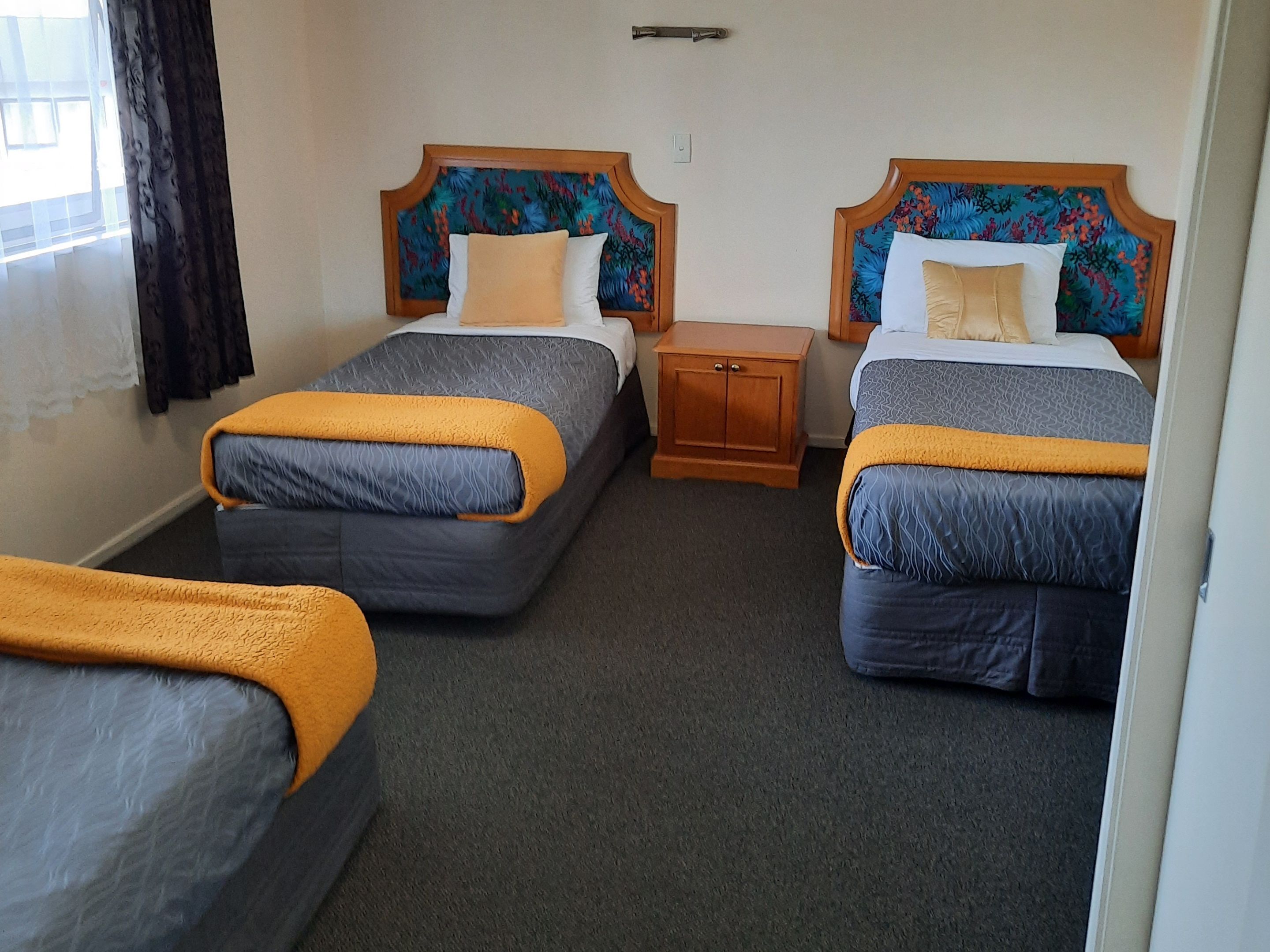 Habitación de hotel con dos camas individuales, cada una con cabecero de madera, una mesita de noche de madera y suelo cubierto de alfombra.