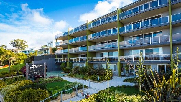 A multi-story hotel with balconies, a landscaped garden, and a sign indicating a vacancy. - Albacore Apartments (Merimbula)