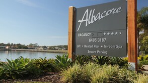 A sign for Albacore accommodation with a vacancy indicator, contact number, and amenities like lift, heated pool, in-room spa, and secure parking. - Albacore Apartments (Merimbula)