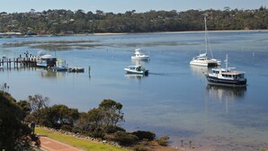 A marina with several boats docked, surrounded by a calm water body and a forested hillside in the background. - Albacore Apartments (Merimbula)