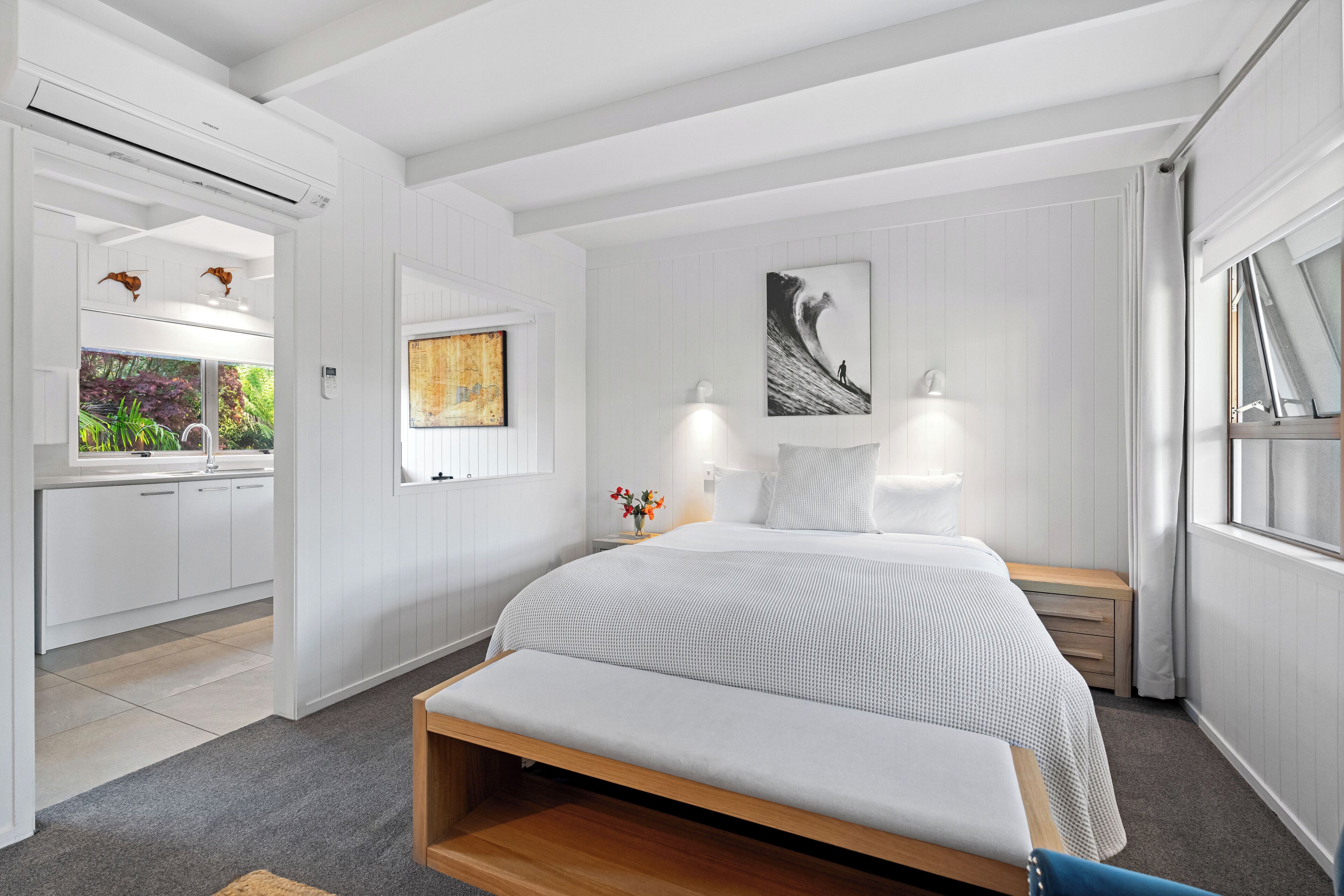 Un dormitorio moderno con una cama grande, mesitas de noche, un banco, una ventana y vistas al baño.
