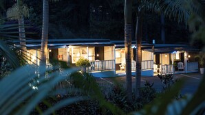 A hotel with a covered outdoor seating area, palm trees, and a well-lit entrance. - Stay Kerikeri Boutique Apartments and Studios (Kerikeri)