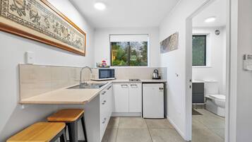 Cocina compacta con microondas, lavamanos y ventana. Hay dos taburetes y un refrigerador pequeño.