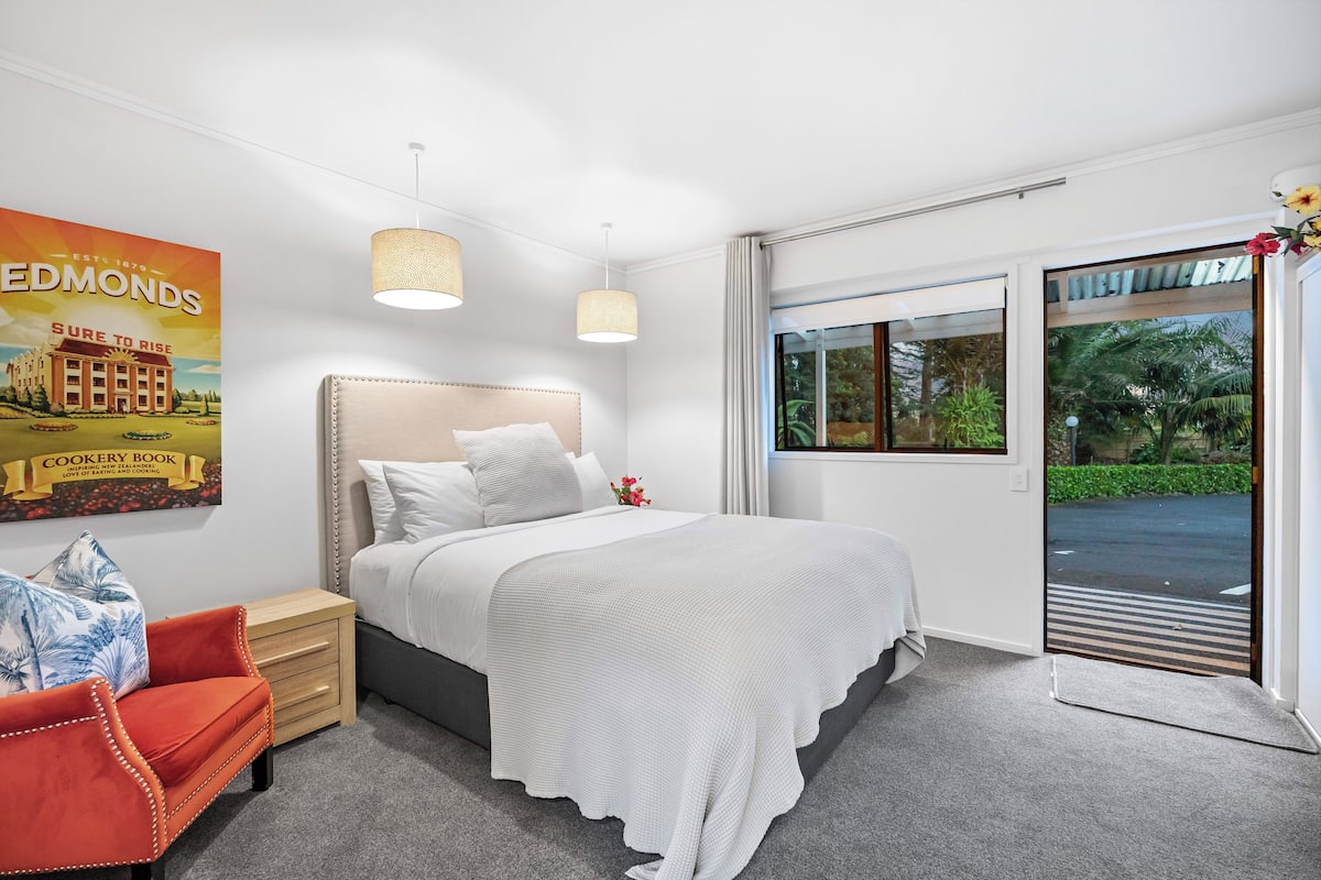 A bedroom with a bed, a nightstand, a chair, a window, and a door.