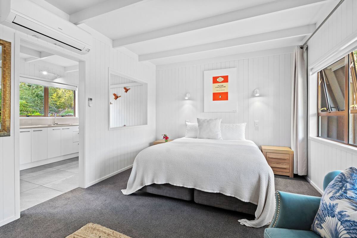 A modern bedroom with a large bed, bedside tables, a nightstand, a window with curtains, and a view of the outdoors.