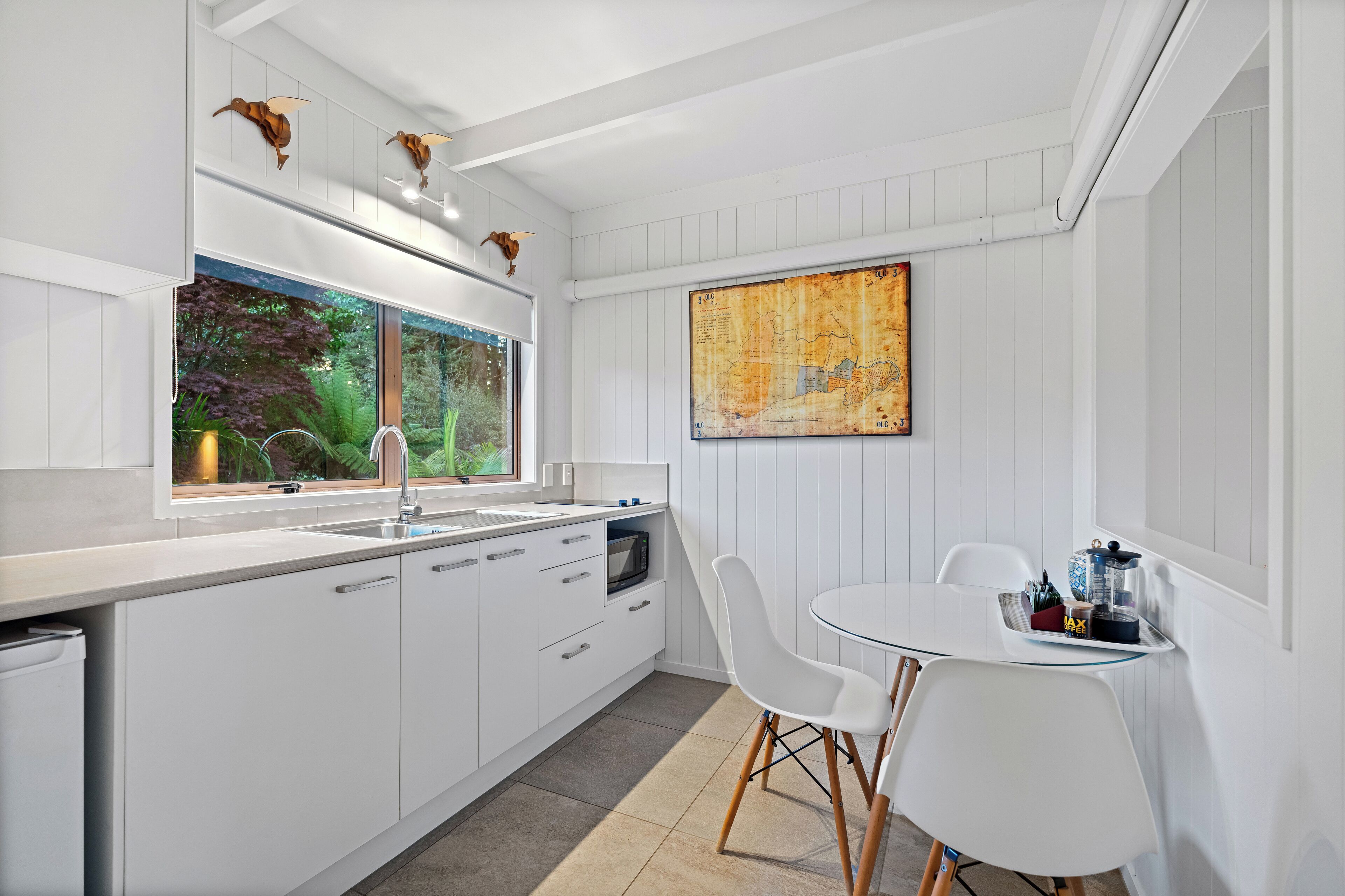 Een moderne keuken met witte kasten, een groot raam en een eethoek met een witte tafel en stoelen.