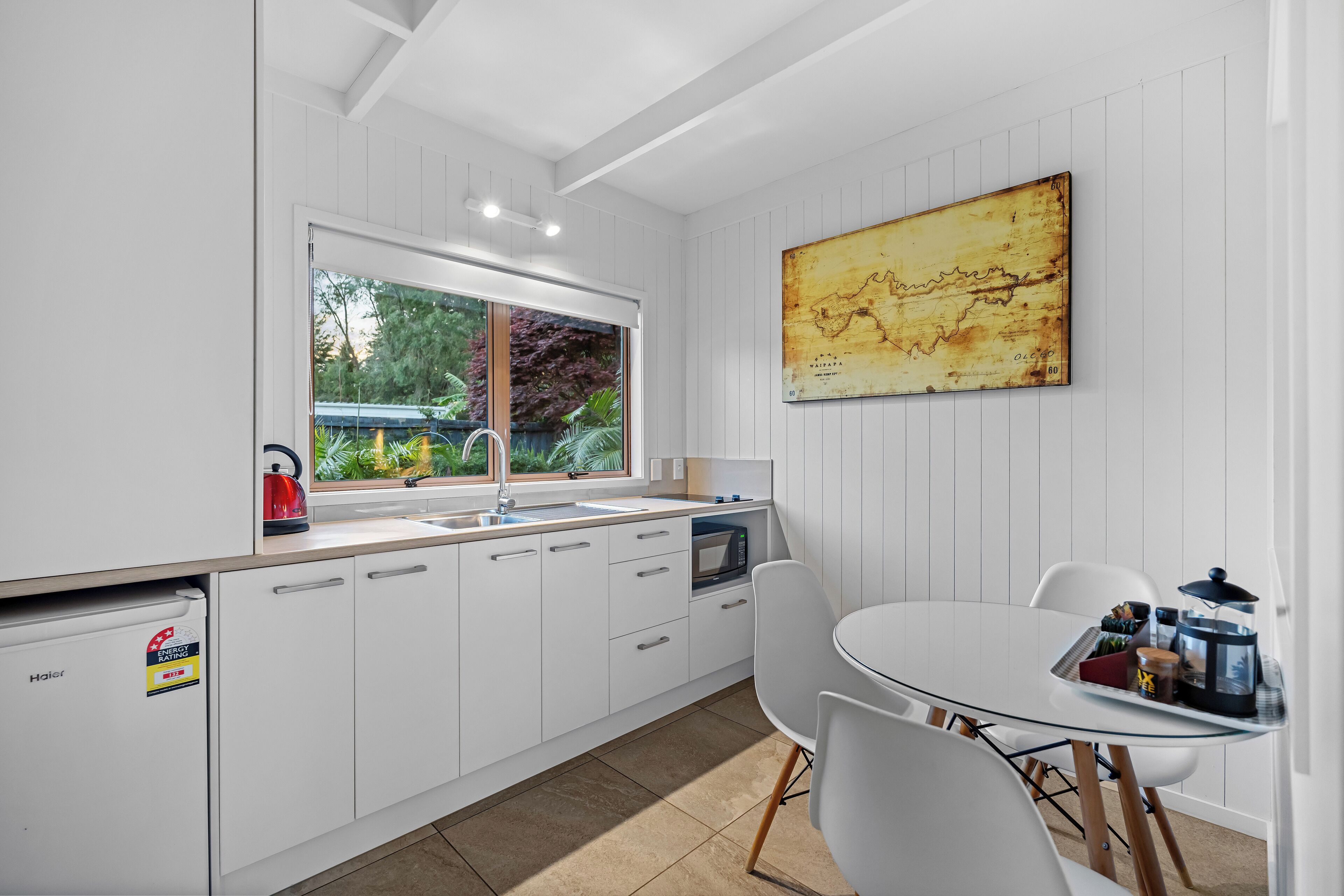 A modern kitchen with white cabinetry, a large window, and a dining area with a glass table.