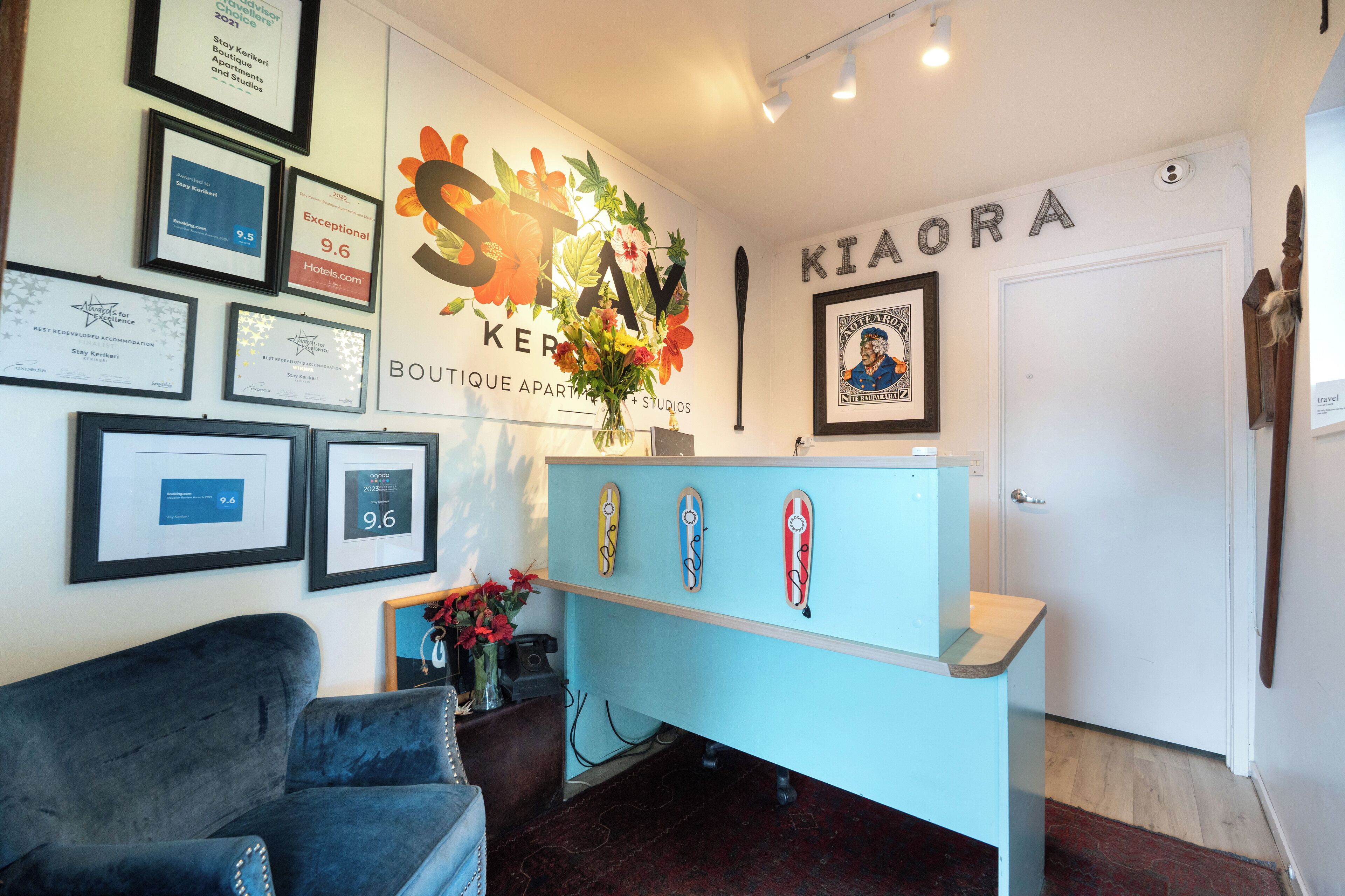 Uma receção com quadros de prémios, uma parede com uma grande decoração floral e uma porta com a inscrição 'KIAORA'.