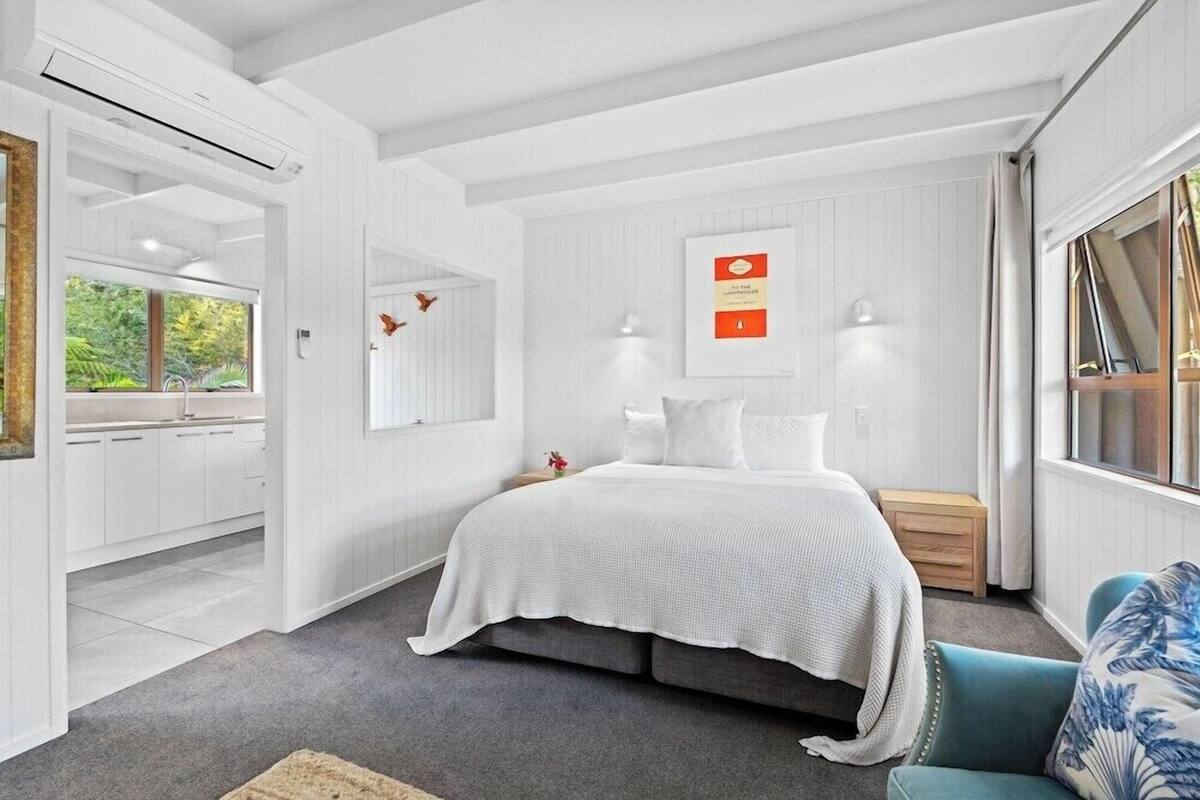 A bedroom with a bed, bedside table, lamp, and a view of the garden.