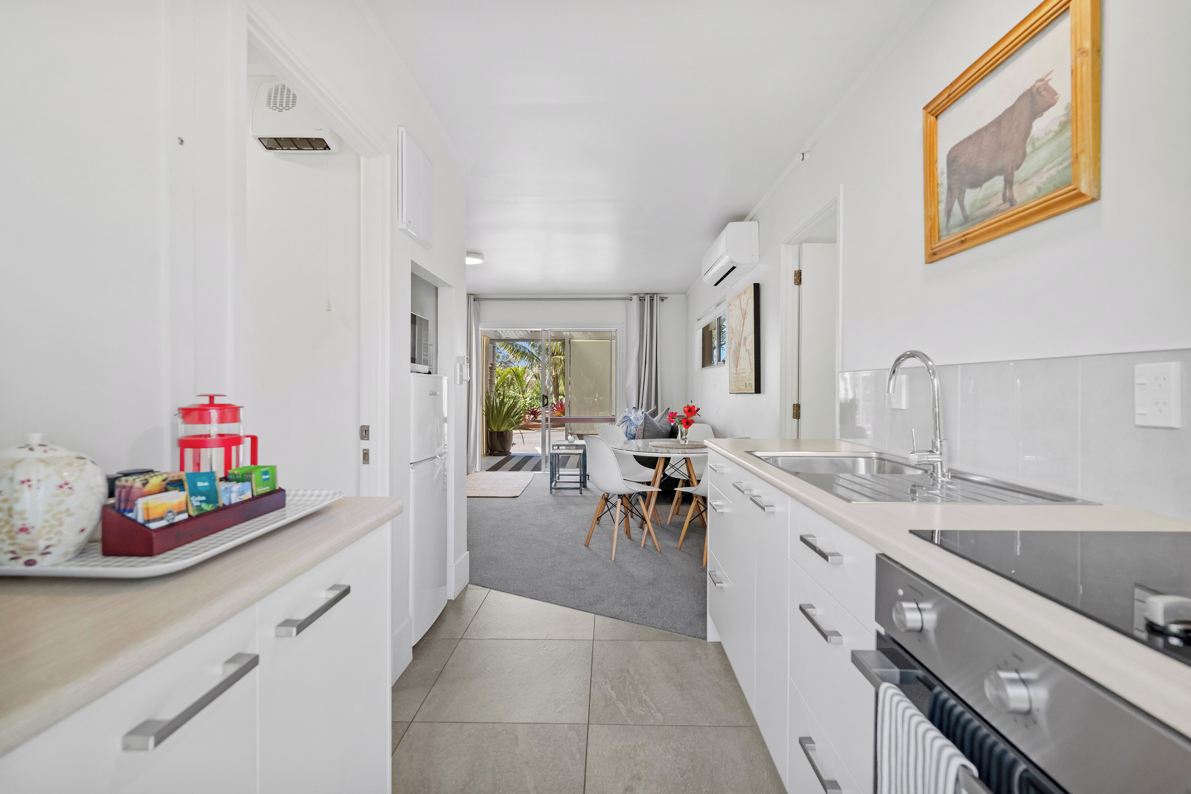 A modern kitchen with white cabinetry, a stainless steel sink, and a dining area with a table and chairs.