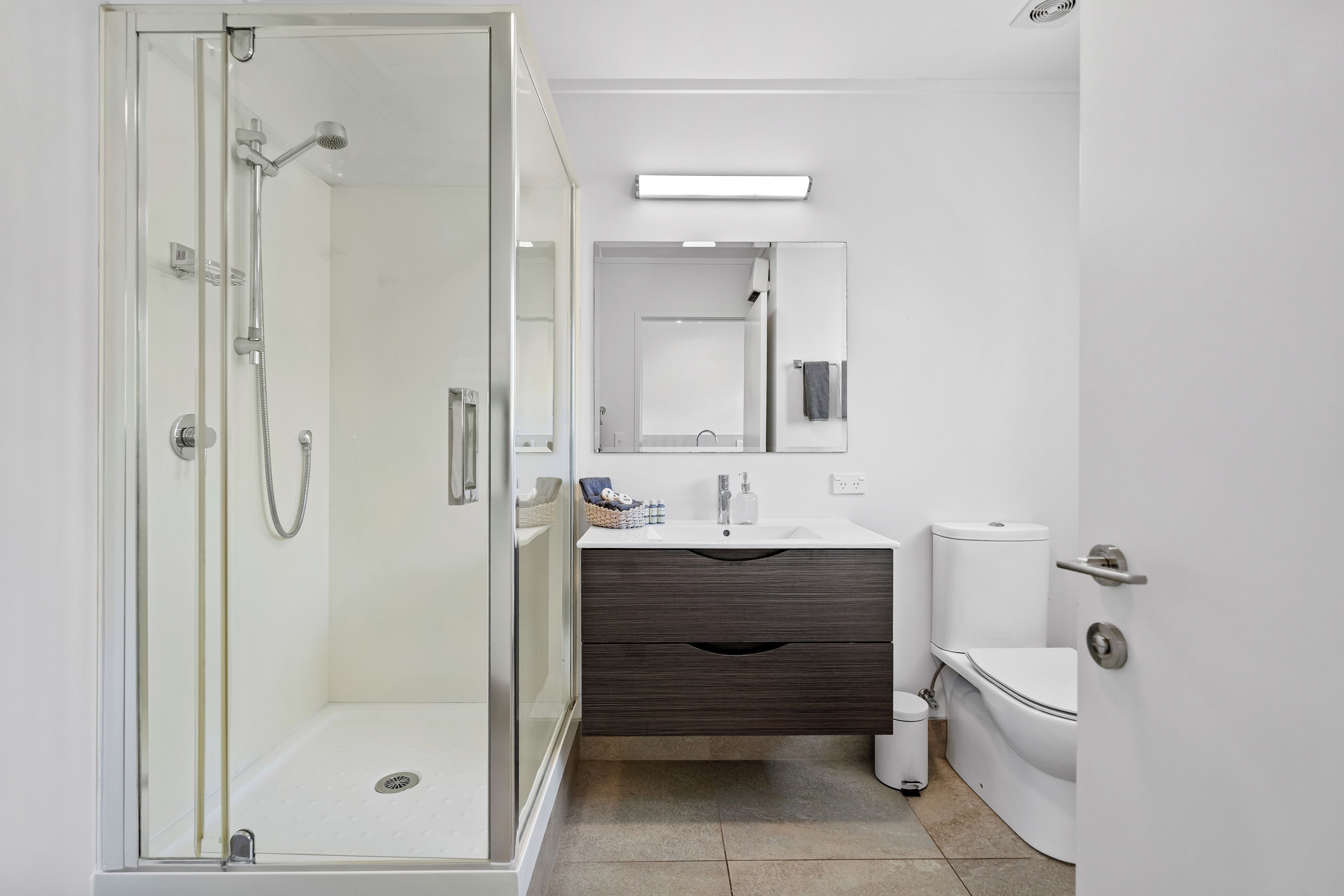 A modern bathroom with a glass-enclosed shower, a white sink, a dark wood vanity, and a toilet.