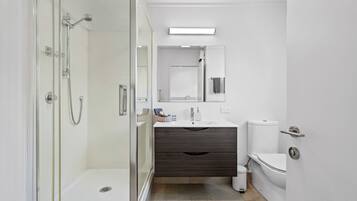 A modern bathroom with a glass-enclosed shower, a white sink, a dark wood vanity, and a toilet.