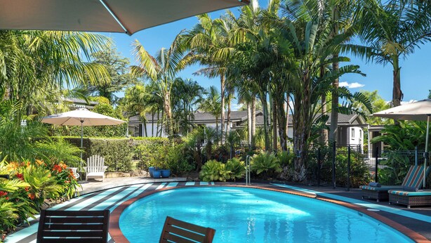 A swimming pool with lounge chairs and umbrellas, surrounded by palm trees and a well-maintained garden. - Stay Kerikeri Boutique Apartments and Studios (Kerikeri)