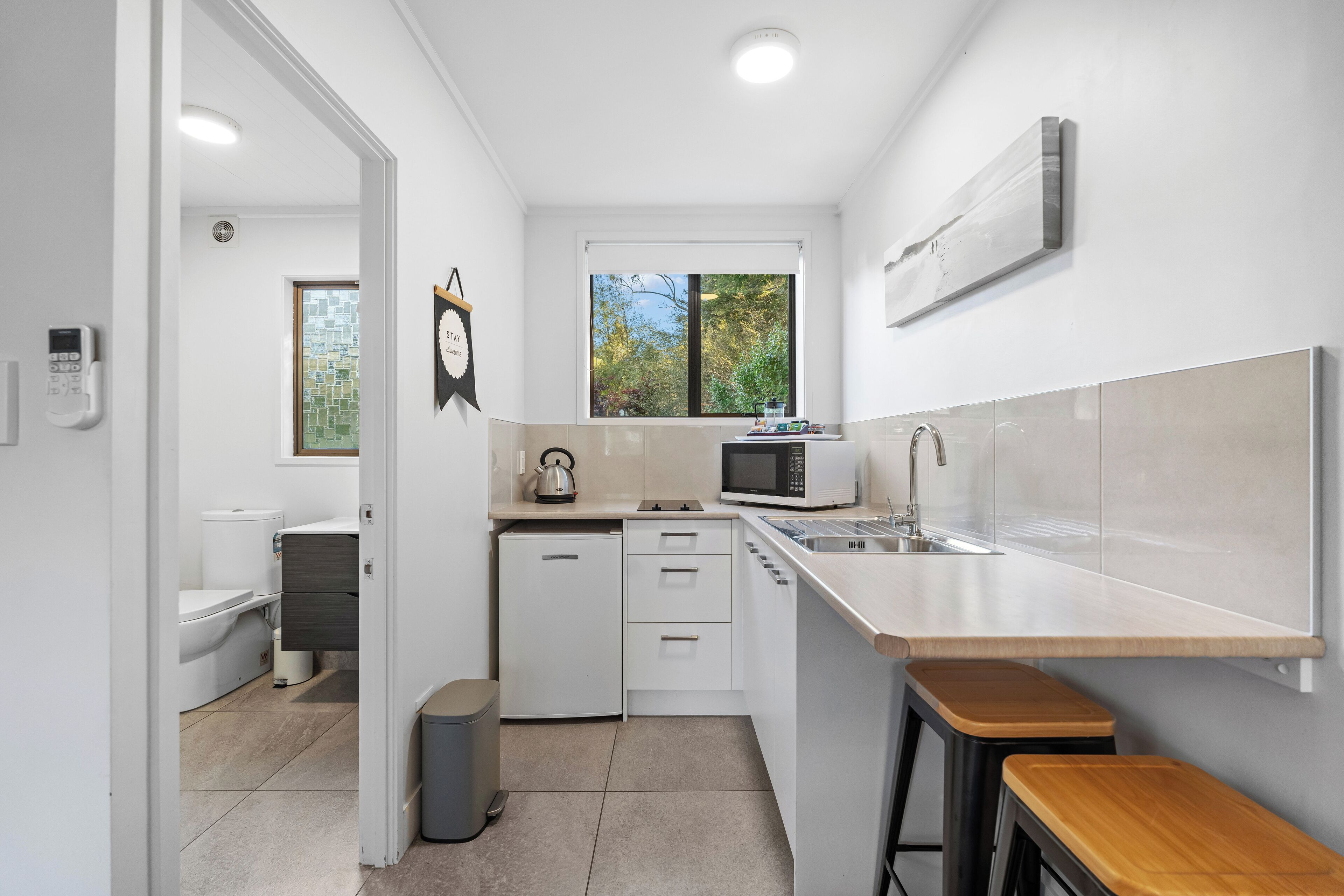 Une cuisine moderne avec des meubles blancs, un four à micro-ondes encastré et une grande fenêtre.
