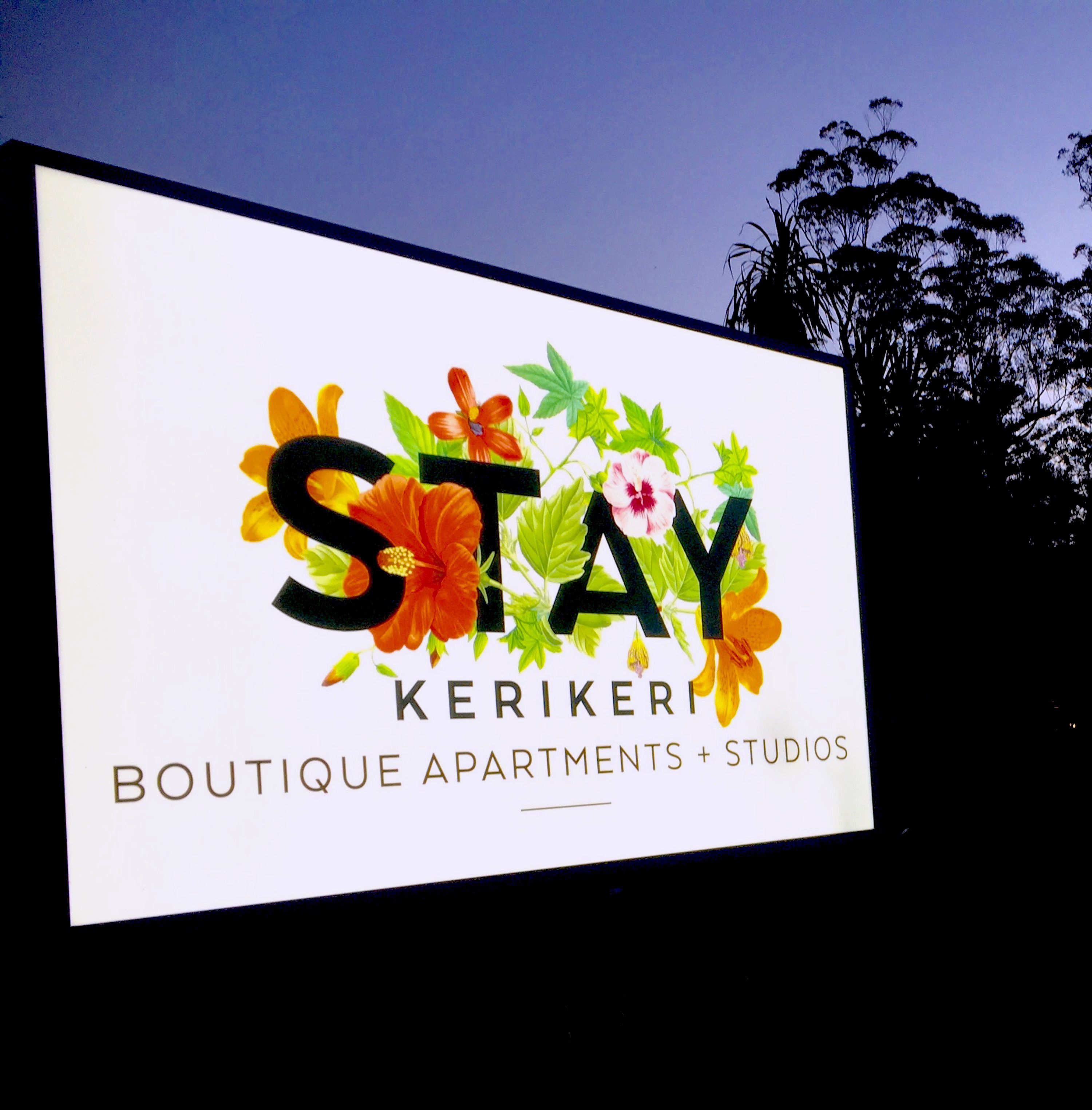 Une enseigne pour « STAY Keriker Boutique Apartments + Studios », agrémentée de décorations florales.
