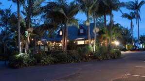 A hotel with a tropical garden, palm trees, and a well-lit exterior at dusk. - Stay Kerikeri Boutique Apartments and Studios (Kerikeri)
