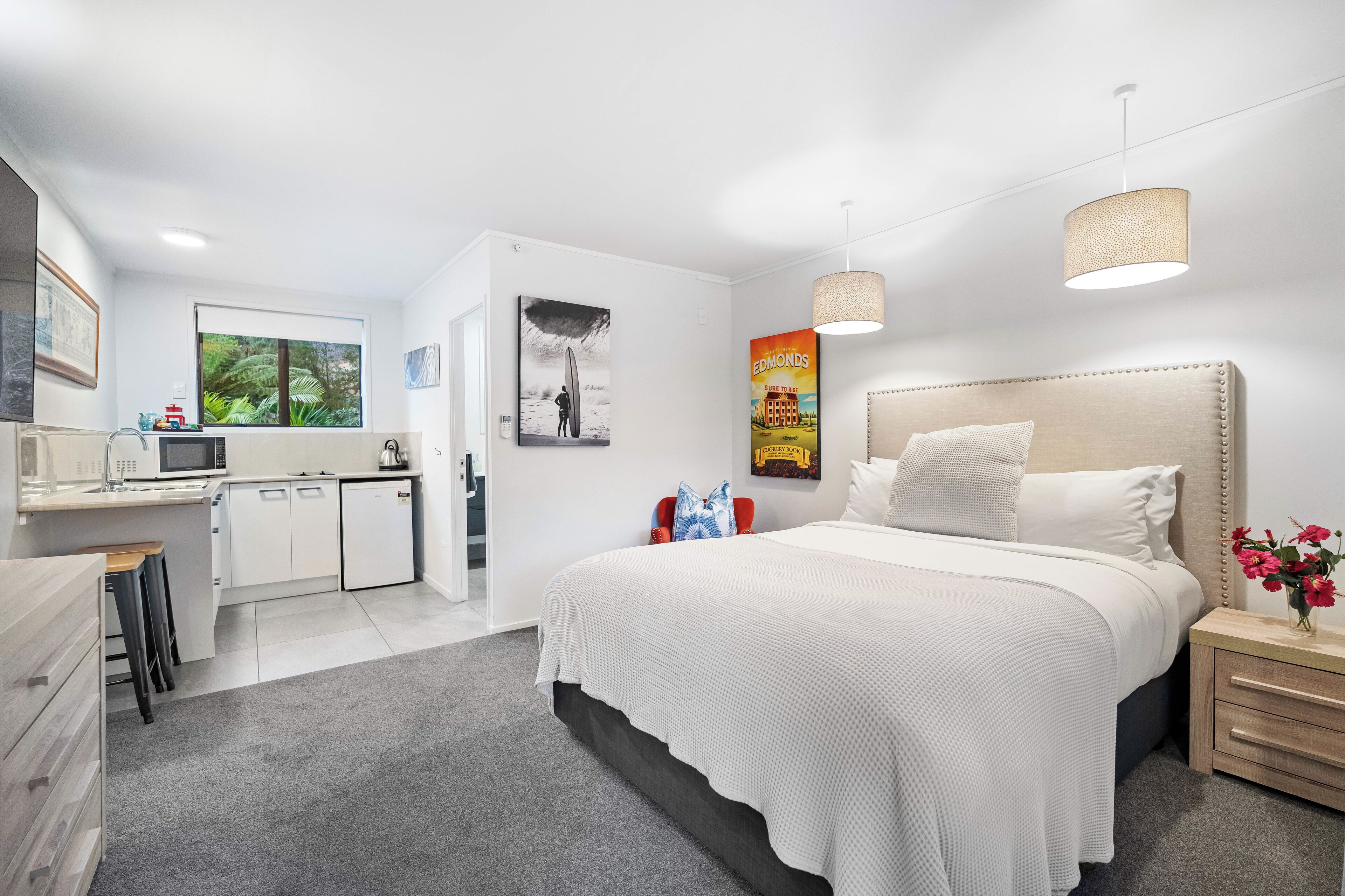 Een moderne slaapkamer met een groot bed, nachtkastjes, een bureau en een kitchenette.