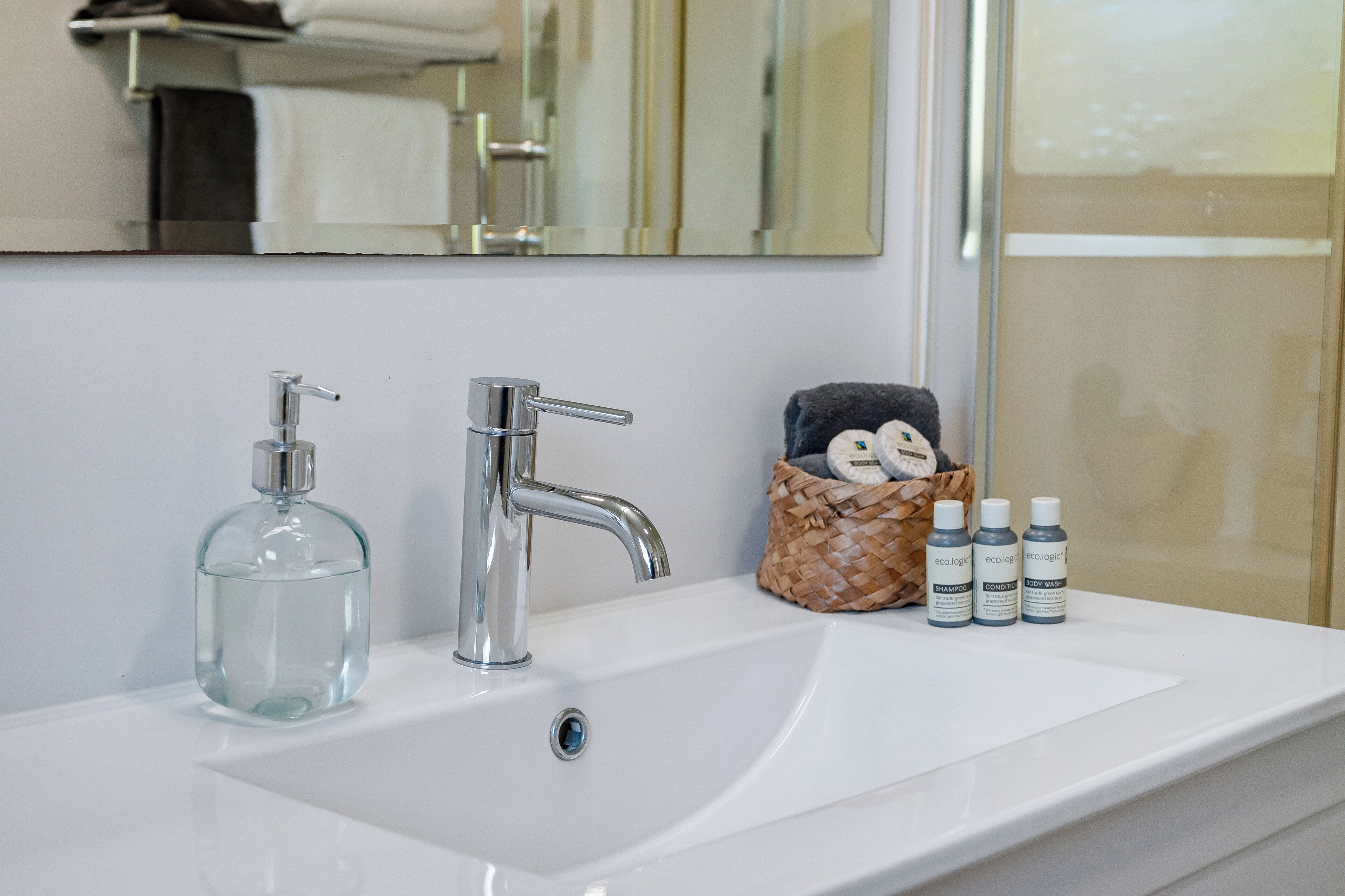 A bathroom sink with a mirror above it, a bottle of liquid soap, a faucet, and three bottles of shampoo and conditioner.