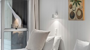 A bedroom with a bed, a window with curtains, a wall-mounted light fixture, and a painting of coconuts. - Stay Kerikeri Boutique Apartments and Studios (Kerikeri)