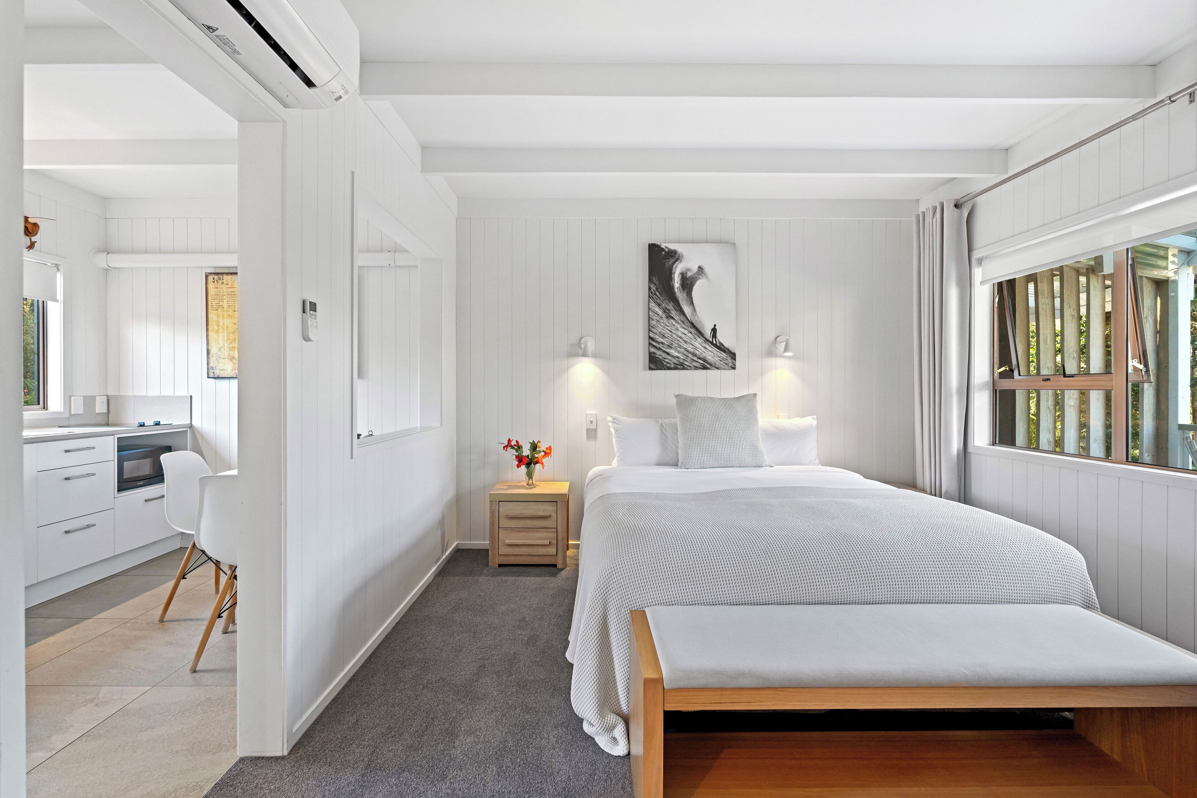 A bedroom with a bed, bedside lamps, a nightstand, a painting, and a window with curtains.