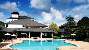 A swimming pool with lounge chairs and umbrellas, surrounded by a building with a covered patio and a large tree. - Alpine Golf Resort Chiang Mai (Ban Thi)