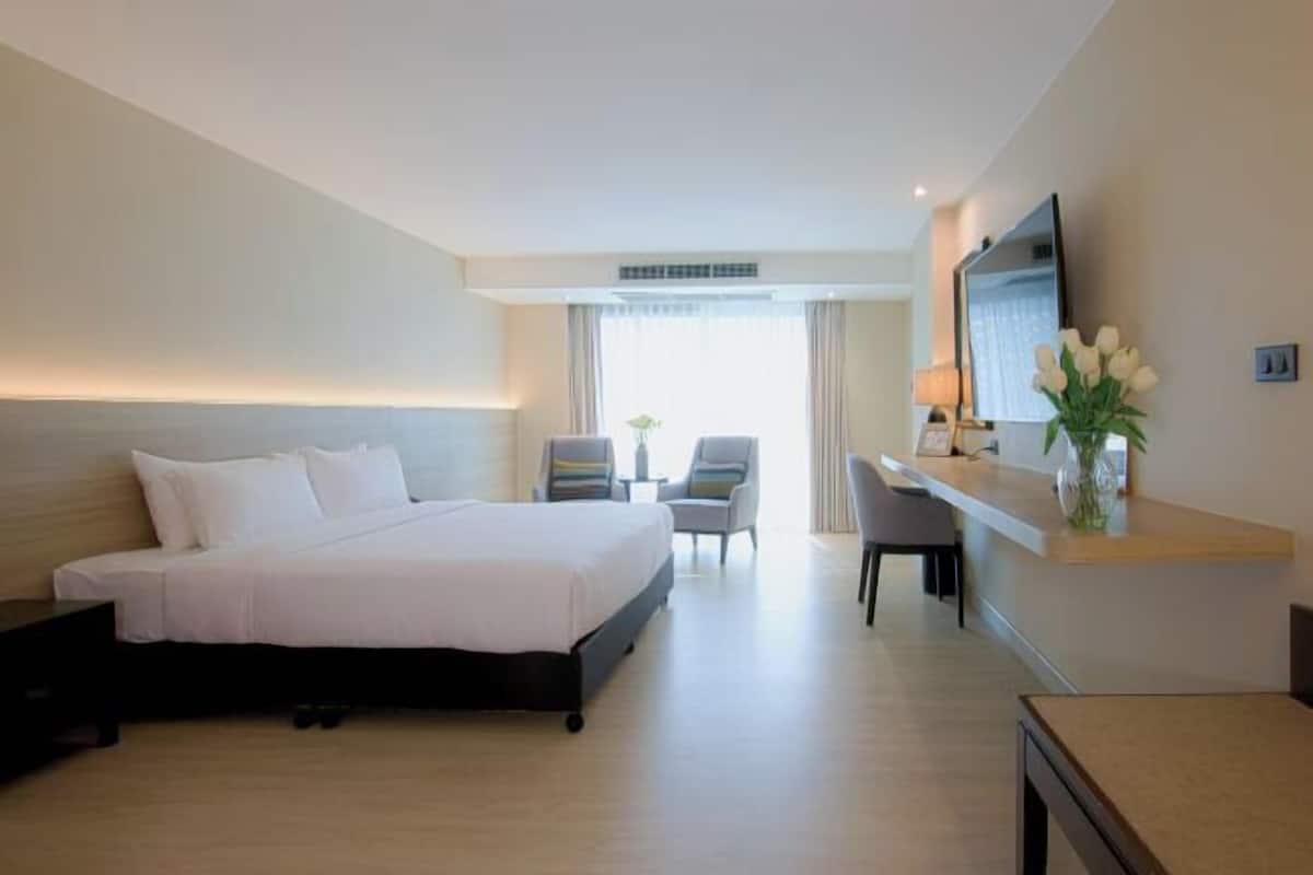 A hotel room with a bed, a desk, a chair, a TV, and a mirror.