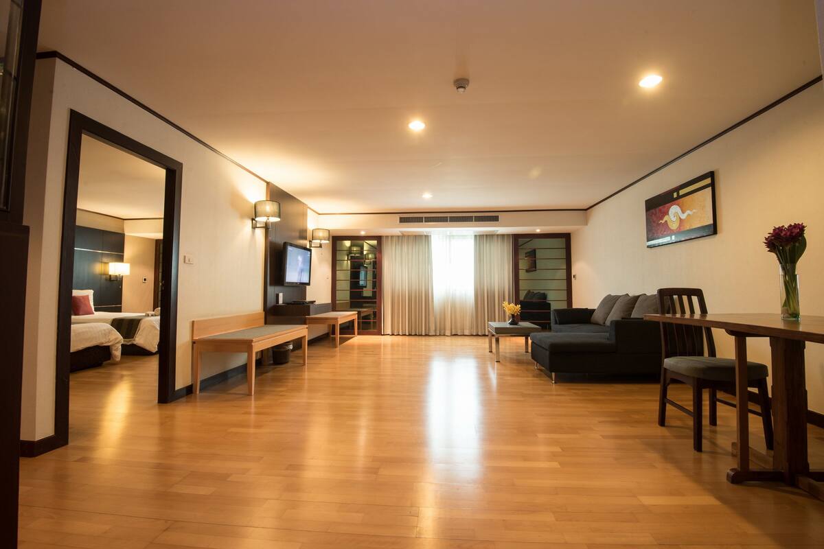 A modern living room with a wooden floor, a sofa, a dining table, and a TV.