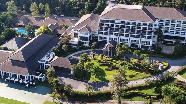 An aerial view of a golf course with a clubhouse, a swimming pool, and a large hotel with multiple floors and a parking area. - Alpine Golf Resort Chiang Mai (Ban Thi)