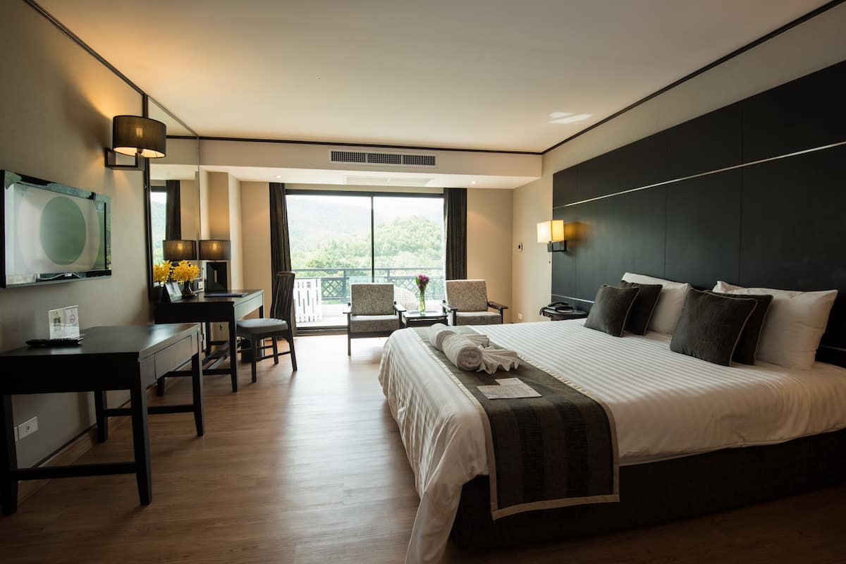 A modern hotel room with a large bed, a desk, and a balcony with chairs.