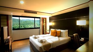 A hotel room with a large bed, a desk, a chair, a lamp, and a view of a mountainous landscape. - Alpine Golf Resort Chiang Mai (Ban Thi)