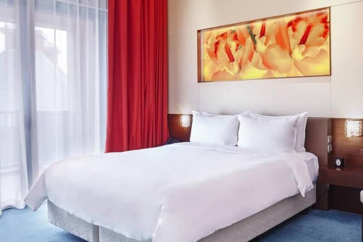 Une chambre d’hôtel avec un grand lit, un rideau rouge et un tableau accroché au mur.