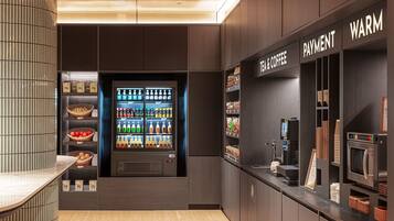 Una cafetería moderna con una máquina expendedora de bebidas, una caja de pago y una estación de café.