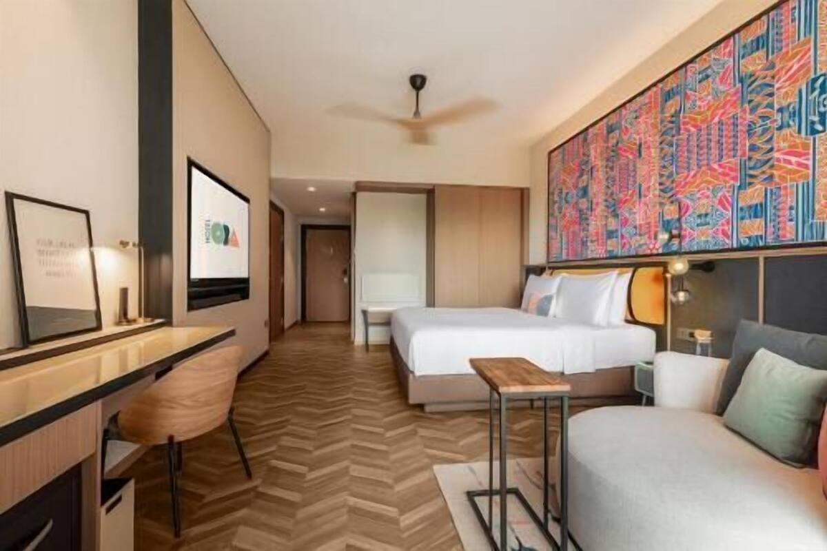 Une chambre d’hôtel avec un lit, un bureau, une chaise et une grande œuvre d’art colorée accrochée au mur.