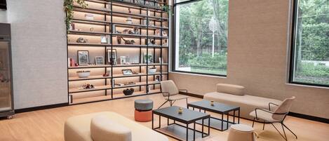 Una sala moderna con una estantería grande, un sofá, dos mesas de centro y vistas a un bosque a través de amplios ventanales.