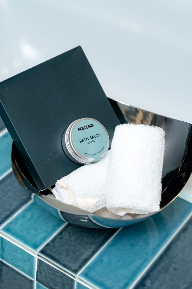 Caixa preta com etiqueta 'POSTCARD BATH SALTS SEA SALTS' e uma toalha branca dentro.