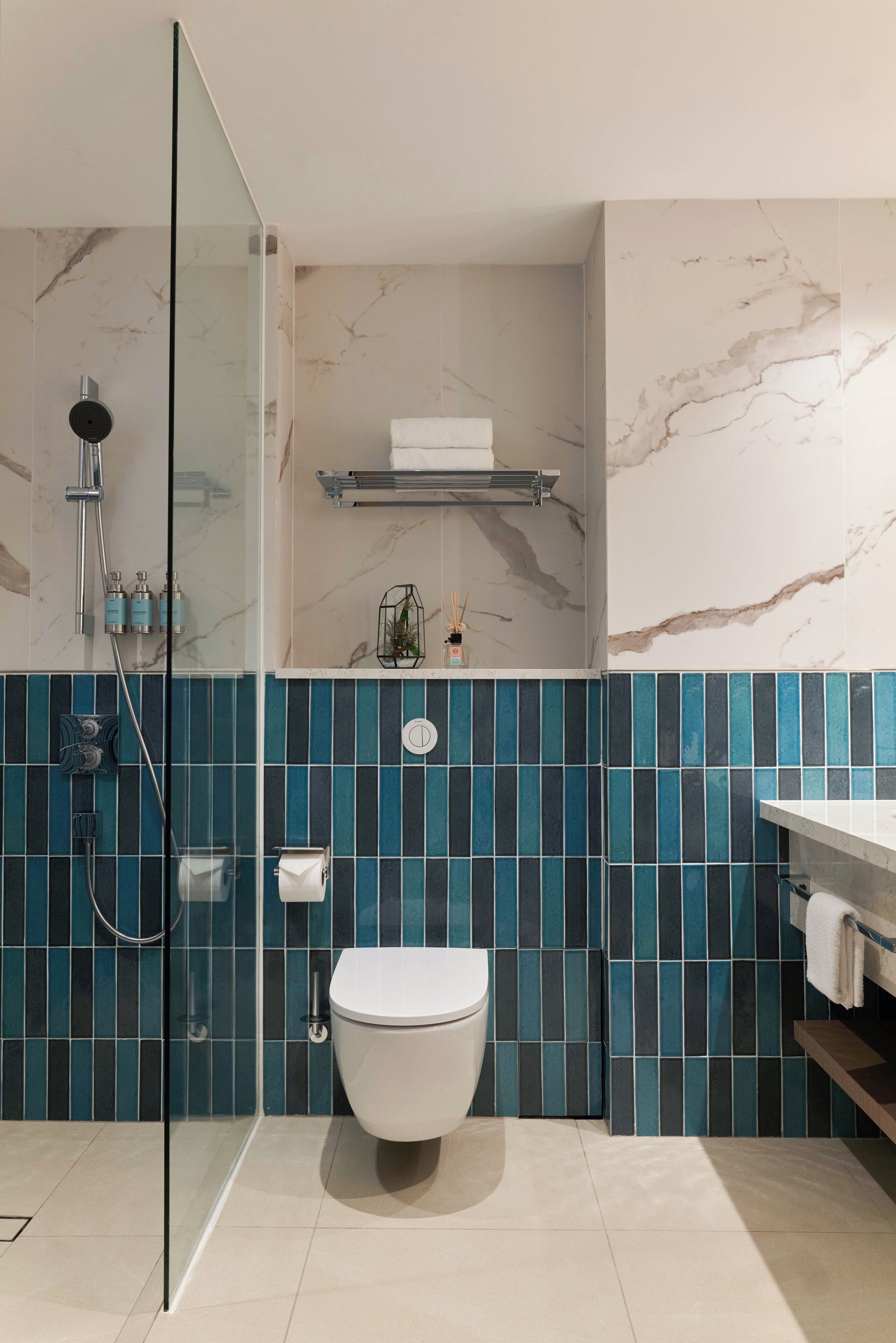 A modern bathroom with a glass-enclosed shower, a white toilet, and blue-tiled walls.
