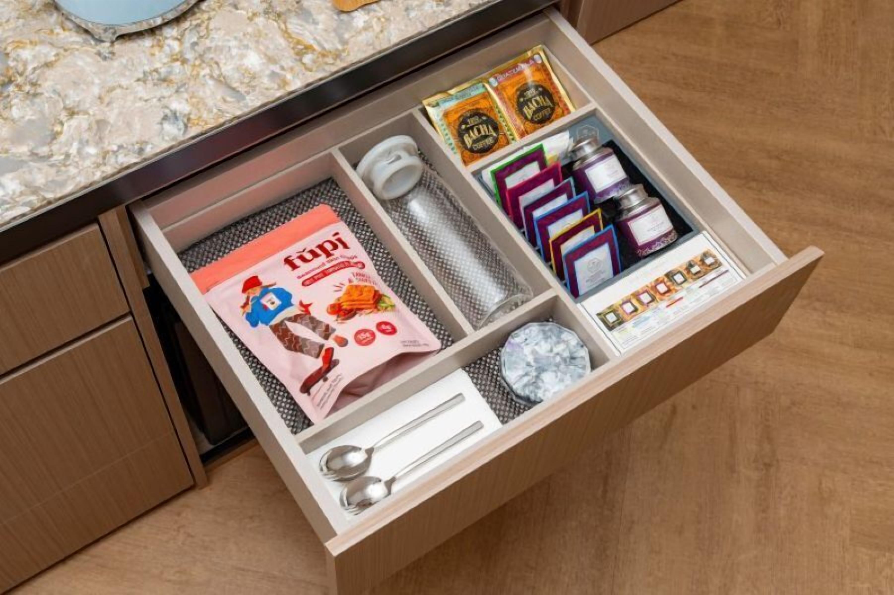 A drawer with various items including a red bag, a water bottle, a spoon, a small container, and some packaged goods.