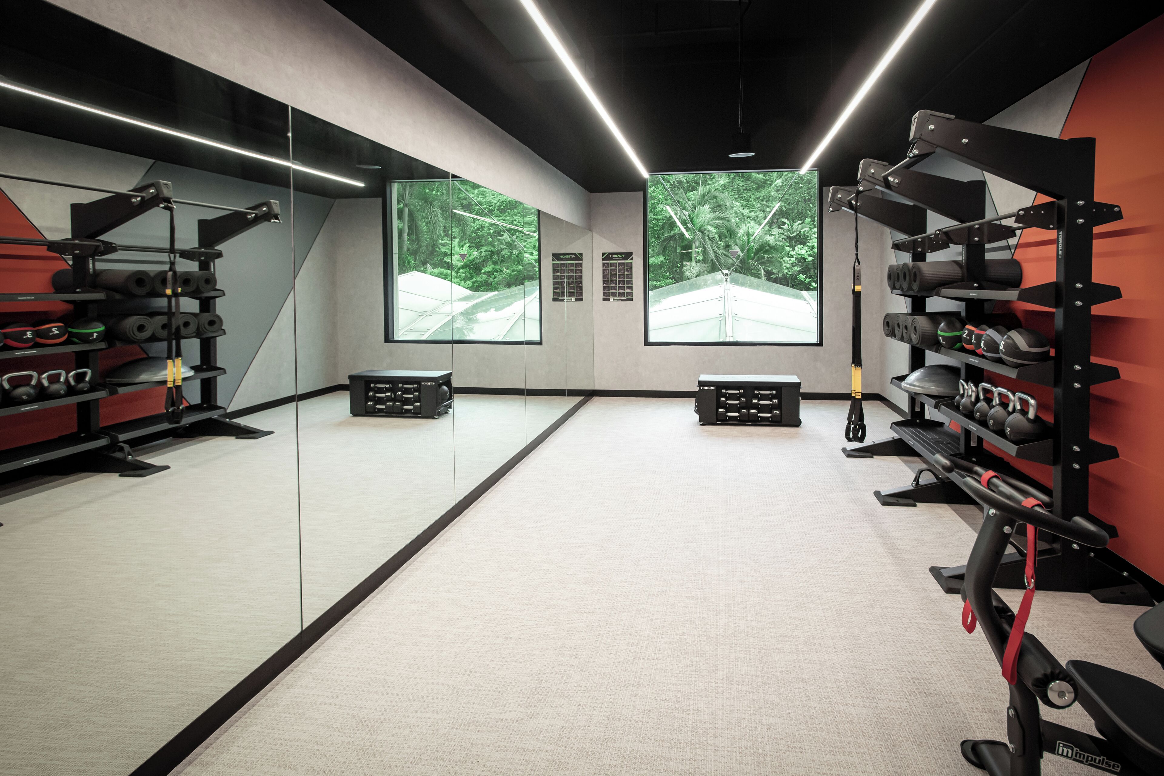 A gym with mirrored walls, exercise equipment, and large windows with a view of greenery.