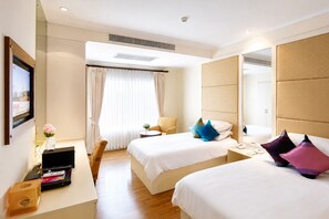 A hotel room with two beds, a desk, a chair, a bedside table, a mirror, and a window with curtains. - Hip Bangkok (Bangkok)