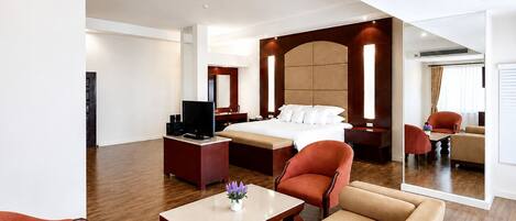 A hotel room with a bed, a desk with a TV, a sofa, and a chair.