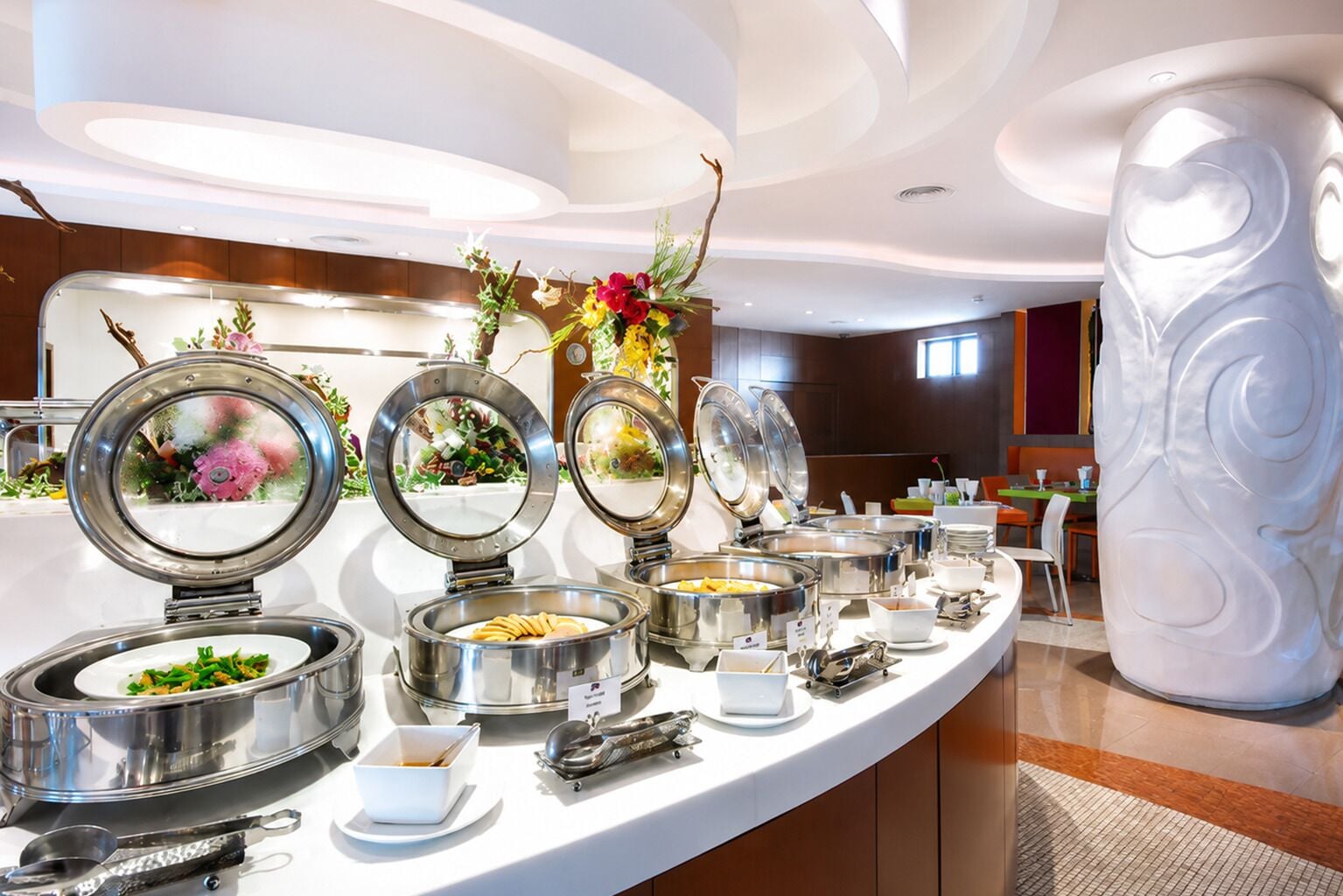 A buffet setup with multiple food stations, including a salad bar and a hot food station, in a modern hotel setting.