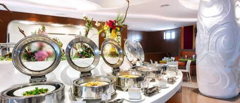 A buffet setup with multiple food stations, including a salad bar and a hot food station, in a modern hotel setting.