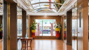 A hotel lobby with a wooden floor, a round table, and two large flower arrangements.