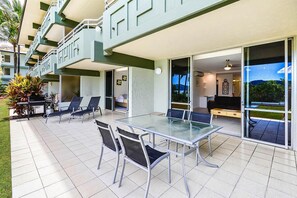Un patio moderno al aire libre con una mesa y sillas de vidrio, una piscina y vistas al océano.