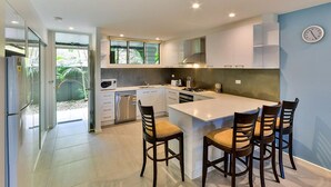 A modern kitchen with a central island, four bar stools, and a large window. - Hibiscus 006 (Whitsundays)