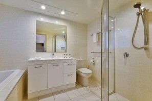 Un baño moderno con ducha separada por mampara de vidrio, tocador blanco con espejo y un inodoro.